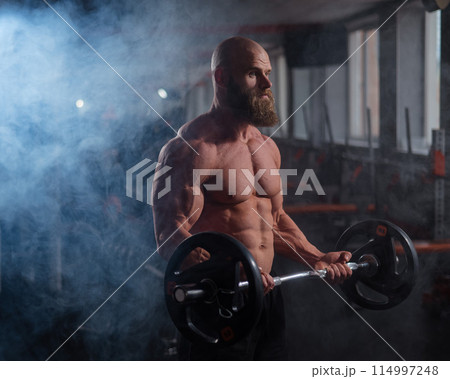 Caucasian bald topless man doing an exercise with a barbell in the gym. Bicep curls with weights. Caucasian bald topless man doing an exercise with a barbell in the gym. Bicep curls with weights. 114997248