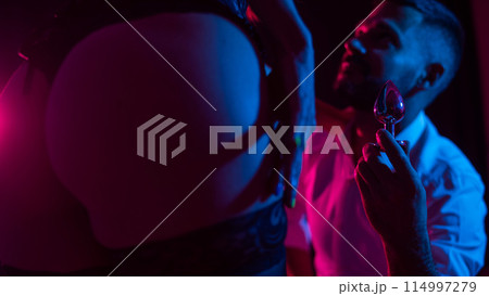 Bearded caucasian man holding an anal plug. Close-up of female buttocks in underwear. Sexual preferences of the couple. Bearded caucasian man holding an anal plug. Close-up of female buttocks in underwear. Sexual preferences of the couple. 114997279