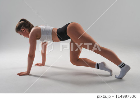 Athletic woman in shorts doing plank exercises on a white background. Athletic woman in shorts doing plank exercises on a white background. 114997330