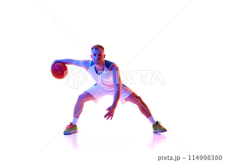 Dynamic portrait of young athlete man in red sportswear training dribbling technique in neon light against white studio background. Dynamic portrait of young athlete man in red sportswear training dribbling technique in neon light against white studio background. 114998380