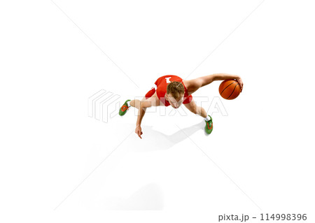 Aerial view of young athletic man, dressed red gear basketball player dribbling in motion against white studio background. Aerial view of young athletic man, dressed red gear basketball player dribbling in motion against white studio background. 114998396