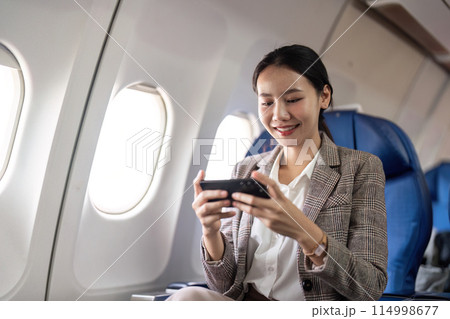 Smiling businesswoman using smartphone on airplane. Concept of in flight communication and business travel 114998677