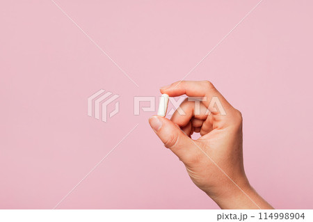 Woman hand holding a white pill against a plain pink background, copy space 114998904
