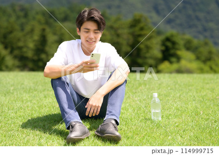 芝生の上でスマホを見る男性 芝生の上でスマホを見る男性 114999715