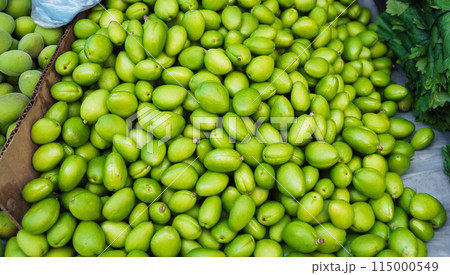 unripe green apricot on counter of a bazaar in Uzbekistan. Traditional Uzbek food on market shelf - green uryuk, dovcha, gura 115000549
