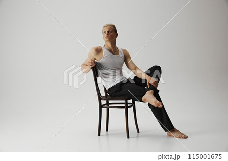 Young handsome man with muscular body posing on chair with thoughtful expression isolated on grey studio background. 115001675