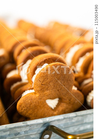 Making gingerbread man cookie sandwiches filled with eggnog buttercream, arrayed on a rustic wooden table, ideal for heartfelt Christmas gifting. Making gingerbread man cookie sandwiches filled with eggnog buttercream, arrayed on a rustic wooden table, ideal for heartfelt Christmas gifting. 115003490