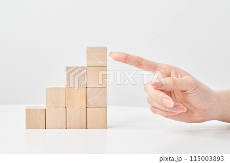 階段状に積まれた木製の積み木と指差す女性の手元 115003893