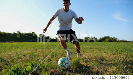 Professional footballer in uniform shows tricks with ball while running at green field. Sportsman kicks ball during jogging at meadow on sunny day. Young man training at stadium. Freestyle football Professional footballer in uniform shows tricks with ball while running at green field. Sportsman kicks ball during jogging at meadow on sunny day. Young man training at stadium. Freestyle football 115006693