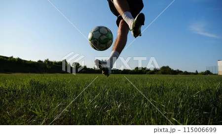 Sportsman juggling soccer ball on stadium at sunny day. Young man kicking ball at green field. Professional footballer practicing tricks at meadow with sunlight at background. Freestyle football. Sportsman juggling soccer ball on stadium at sunny day. Young man kicking ball at green field. Professional footballer practicing tricks at meadow with sunlight at background. Freestyle football. 115006699