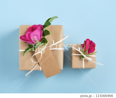 Two brown gift boxes with rosehip flowers and white ribbon on blue background. Two brown gift boxes with rosehip flowers and white ribbon on blue background. 115006966