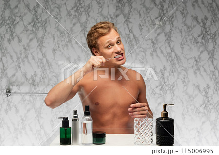 Portrait of young handsome, shirtless man brushing teeth in bath against marbled wall. Dental health. Concept of beauty and self care. Portrait of young handsome, shirtless man brushing teeth in bath against marbled wall. Dental health. Concept of beauty and self care. 115006995