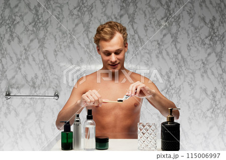 Portrait of young man preparing to brushing teeth with toothpaste applying in on toothbrush against marbled wall. 115006997