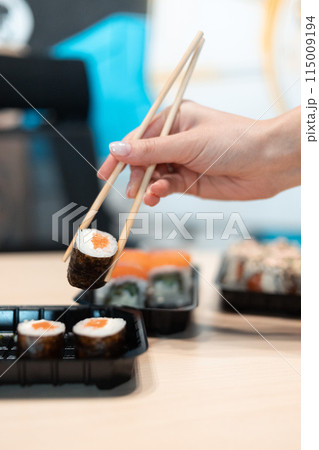 Sushi delivery. Set of rolls in a disposable box on a black background. Top view 115009194