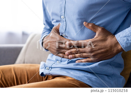 A man is seen clutching his stomach, indicating abdominal pain or discomfort. He is sitting down and appears to be in distress, suggesting a possible gastrointestinal issue or stomach ache. 115010258
