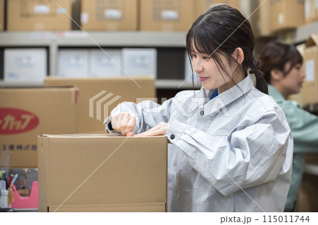 梱包作業する作業着姿の若い女性 梱包作業する作業着姿の若い女性 115011744