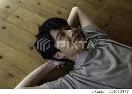 フローリングに寝そべる男性 115013577
