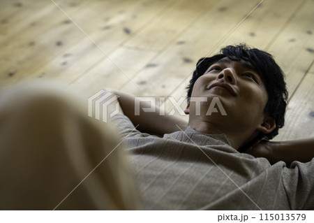 フローリングに寝そべる男性 115013579