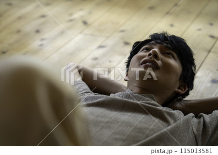 フローリングに寝そべる男性 115013581