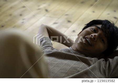 フローリングに寝そべる男性 115013582