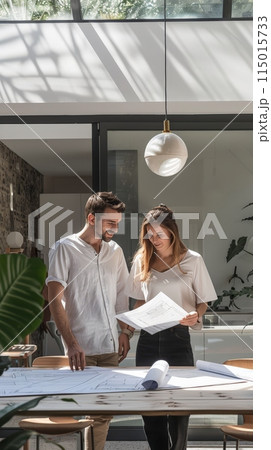Young couple reviewing architectural blueprints in a modern office. Real estate project planning and teamwork concept. Young couple reviewing architectural blueprints in a modern office. Real estate project planning and teamwork concept. 115015733