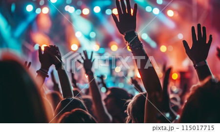 Enthusiastic concert crowd with hands raised under vibrant stage lighting. Captures the energy and excitement of live music performances and festivals. 115017715