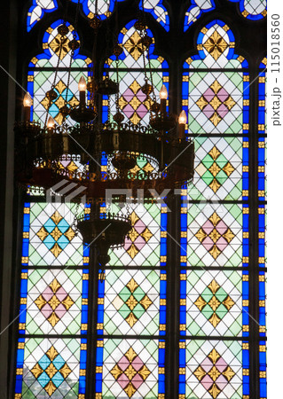 Stained glass windows with chandelier in gothic church, displaying vibrant colorful patterns 115018560