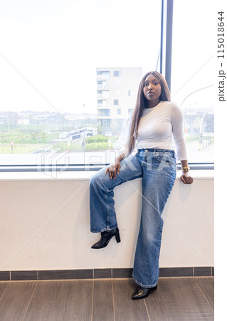 A confident woman in casual chic attire, enjoying a beautiful view from her office window 115018644