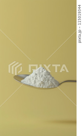 Spoonful of powdered sugar substitute against a yellow background. Suitable for healthy diet and low-calorie sweetener concepts. 115019344