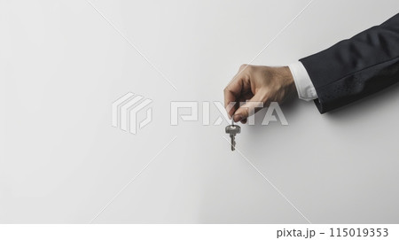 Hand holding a house key against a white background. Concept of real estate, property ownership, and investment. 115019353