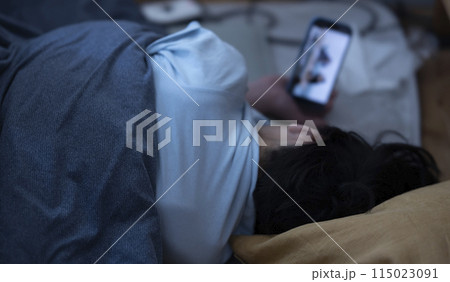 布団でスマホを見る子ども 115023091