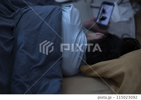 布団でスマホを見る子ども 布団でスマホを見る子ども 115023092
