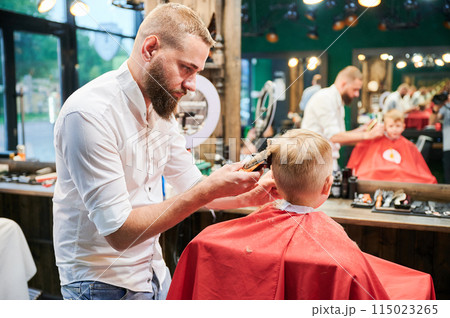 Barber using comb and shaver to cut hair. Professional hairdresser shaving little kid's nape. Barber using comb and shaver to cut hair. Professional hairdresser shaving little kid's nape. 115023265