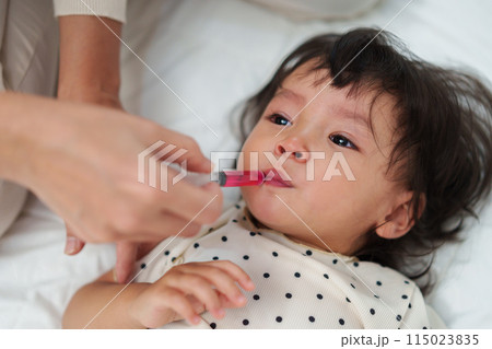 mother feeding liquid medicine to baby girl by syringe. sick crying toddler 115023835