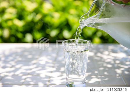 水を注ぐ 木陰のテーブルで冷たいミネラルウォーターを飲む 水を注ぐ 木陰のテーブルで冷たいミネラルウォーターを飲む 115025246