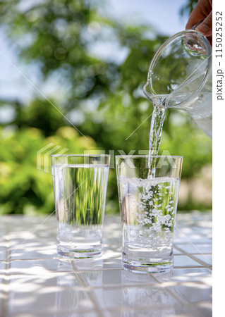 水を注ぐ　木陰のテーブルで冷たいミネラルウォーターを飲む 115025252