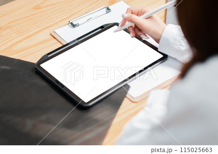 A woman is writing on a tablet with a pen. The tablet is on a desk with a clipboard and a piece of paper. The woman is wearing a white shirt and she is focused on her work A woman is writing on a tablet with a pen. The tablet is on a desk with a clipboard and a piece of paper. The woman is wearing a white shirt and she is focused on her work 115025663