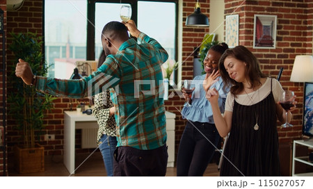 Young adults of various nationalities dancing at home party while drinking alcohol. Friends hanging around, having good time together while enjoying upbeat music in living room Young adults of various nationalities dancing at home party while drinking alcohol. Friends hanging around, having good time together while enjoying upbeat music in living room 115027057