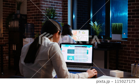 Worker looks over statistical data financial graphs on laptop screen, researching key data for company project. Businesswoman analyzing stock market figures and charts on electronic device, camera A 115027175