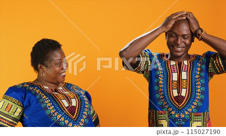Joyful african american people laughing at something in studio, having fun with jokes and being amused over orange background. Married couple enjoying laugh on camera, silly partners. Joyful african american people laughing at something in studio, having fun with jokes and being amused over orange background. Married couple enjoying laugh on camera, silly partners. 115027190