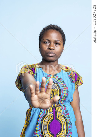 African american serious person doing stop sign with her palm, expressing rejection and negativity. Young woman raising hand and presenting refusal and disappointment, displeased girl. African american serious person doing stop sign with her palm, expressing rejection and negativity. Young woman raising hand and presenting refusal and disappointment, displeased girl. 115027228
