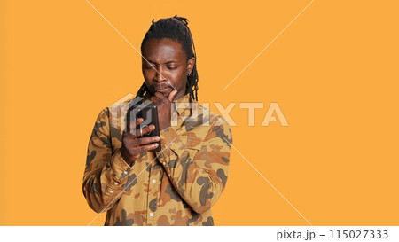 Modern guy navigating online websites on smartphone, checking his chats for texts and posing on camera. African american person using mobile apps to stay connected with friends. Handheld shot. 115027333