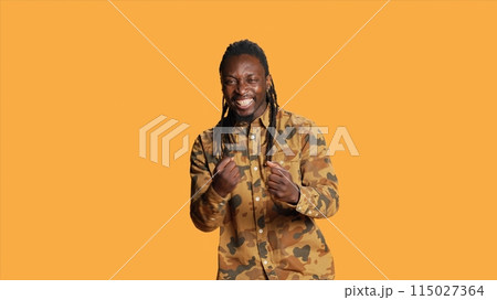 Joyful person cheering at something on camera, feeling happy and applauding for victory. African american adult clapping hands and celebrating win, positive optimistic man in studio. 115027364