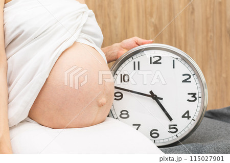 Pregnant woman sitting with clock Pregnant woman sitting with clock 115027901