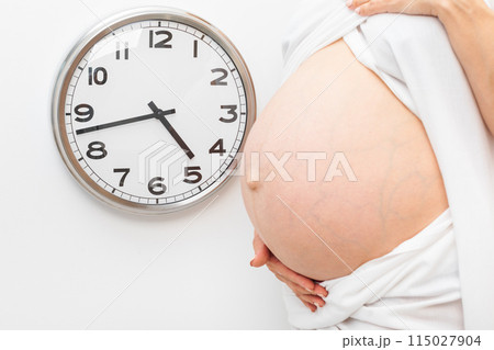Pregnant Woman Holding Belly Next to Wall Clock 115027904