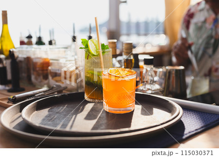Cocktail drinks served in glasses with drinking straws on top counter bar. 115030371