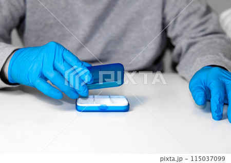 Man in surgical groves with pill organizer. Man in surgical groves with pill organizer. 115037099