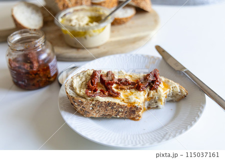 Piece of bread with hummus and sun-dried tomatoes on a white plate 115037161