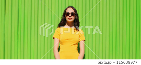 Portrait beautiful young brunette woman model posing in yellow dress on bright green background 115038977