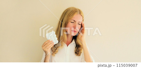 Sick exhausted young woman holding pills, tired girl with headache 115039007